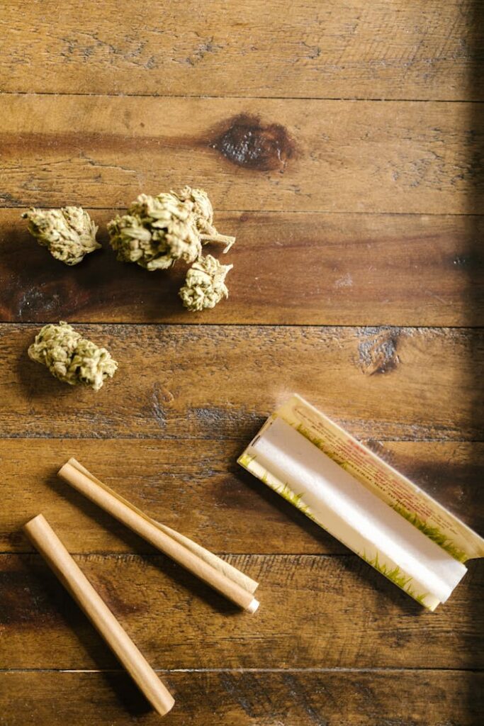 Close-up of cannabis buds with rolling papers on a rustic wooden table.